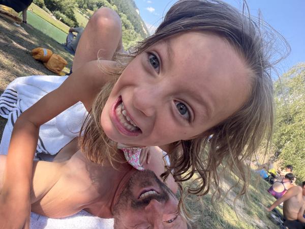 A playful moment is captured between a child and an adult, both smiling broadly, on a sunny day at Rue du Lac, Bozel